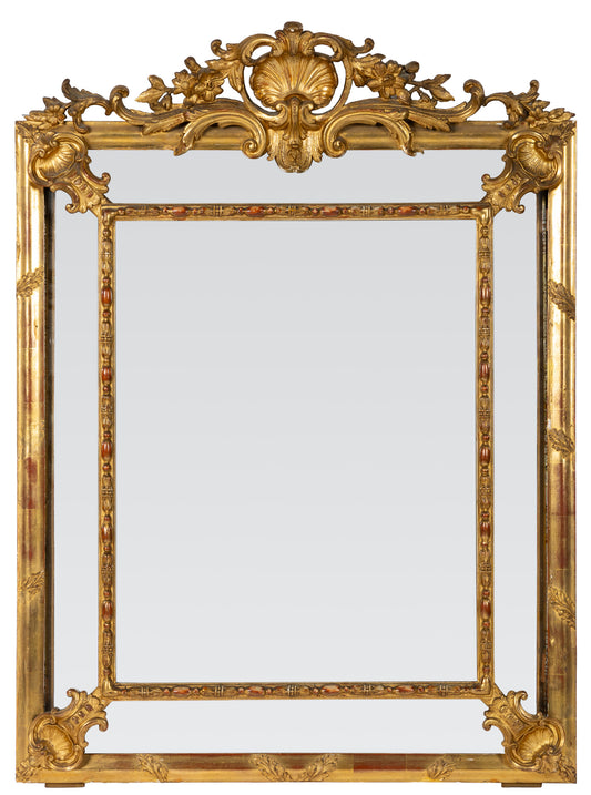 Antique French Rococo-style mirror, likely late 19th to early 20th century with ornate giltwood frame, elaborate crest and aged patina with red accents from Provence