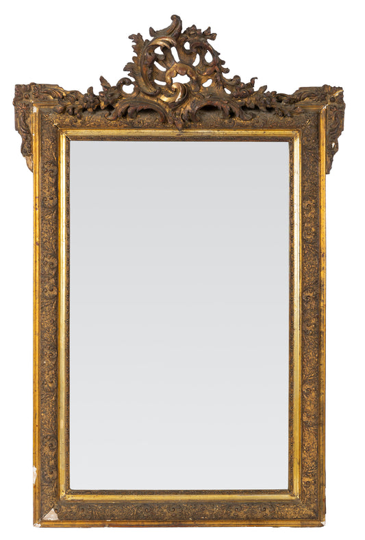 Ornately carved giltwood Louis XV-style mirror with Rococo detailing and a dramatic crest with intricate detailing throughout the frame. Found in Provence
