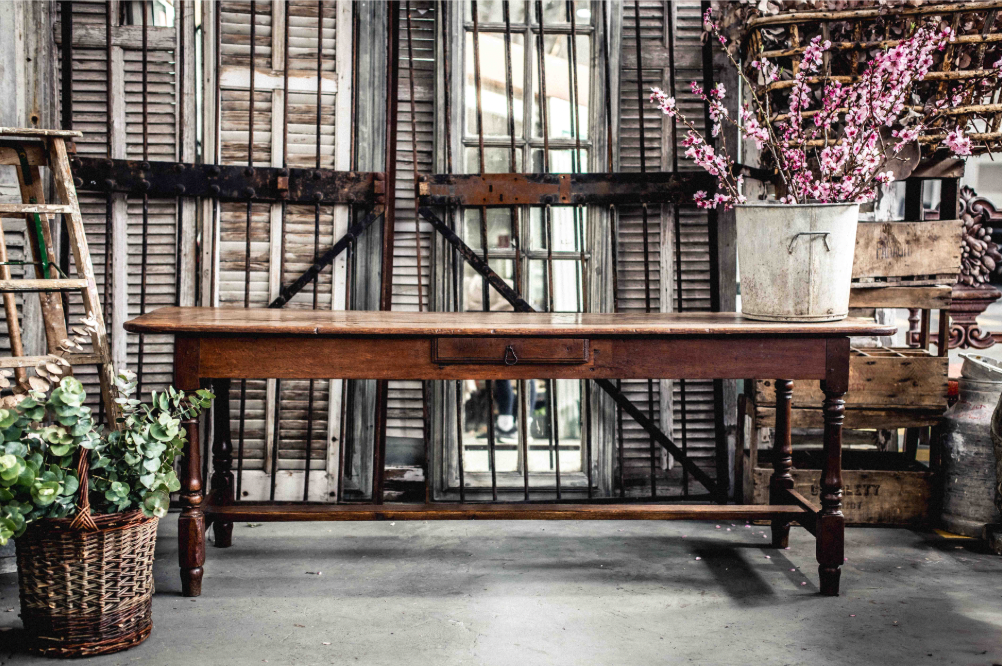 A beautifully aged antique French table with central drawer, curved edges, turned legs and central stretcher bar