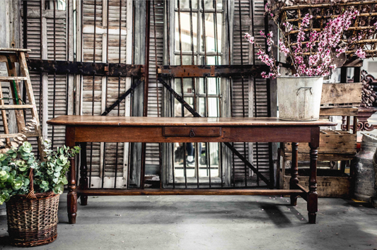 A beautifully aged antique French table with central drawer, curved edges, turned legs and central stretcher bar